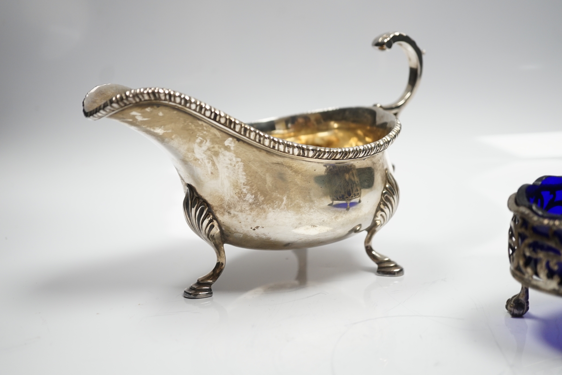 A late Victorian silver sauceboat, with flying scroll handle, William Hutton & Sons, London, 1898 and a George III pierced silver oval salt, with blue glass liner, London, 1768, 12.2oz.